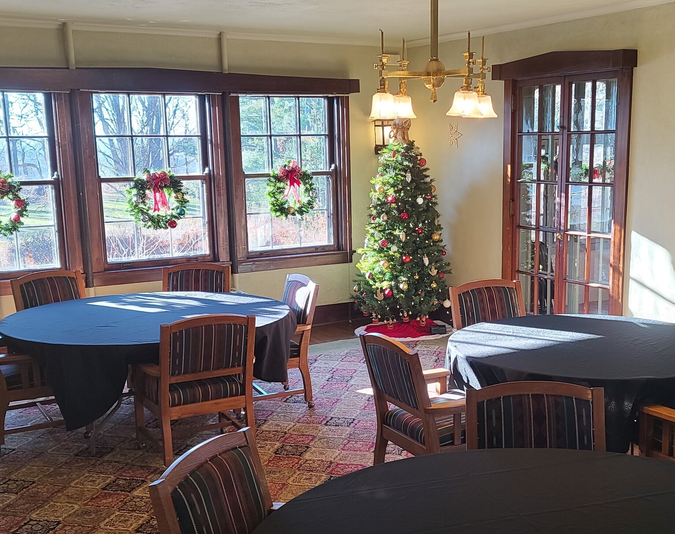 A dining area with a Christmas tree, wooden chairs, and a table with a black tablecloth.