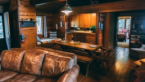 A cozy cabin interior with a leather sofa, wooden dining table, and a kitchen area. - Four Mounds Inn (Dubuque)