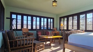A room with large windows, a bed, a wooden table, and wicker furniture. - Four Mounds Inn (Dubuque)