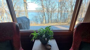 A window seat with a view of a lake and trees, a small table with a plant, and two patterned chairs. - Four Mounds Inn (Dubuque)