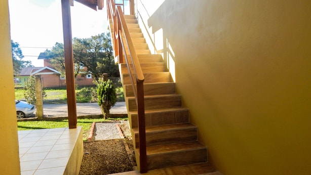 Una escalera de madera que sube a un nivel superior, con vistas a una zona residencial y un coche aparcado al fondo.