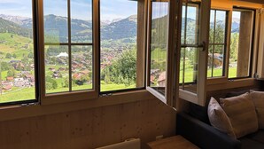 A room with large windows offering a view of a mountainous landscape and a village below.