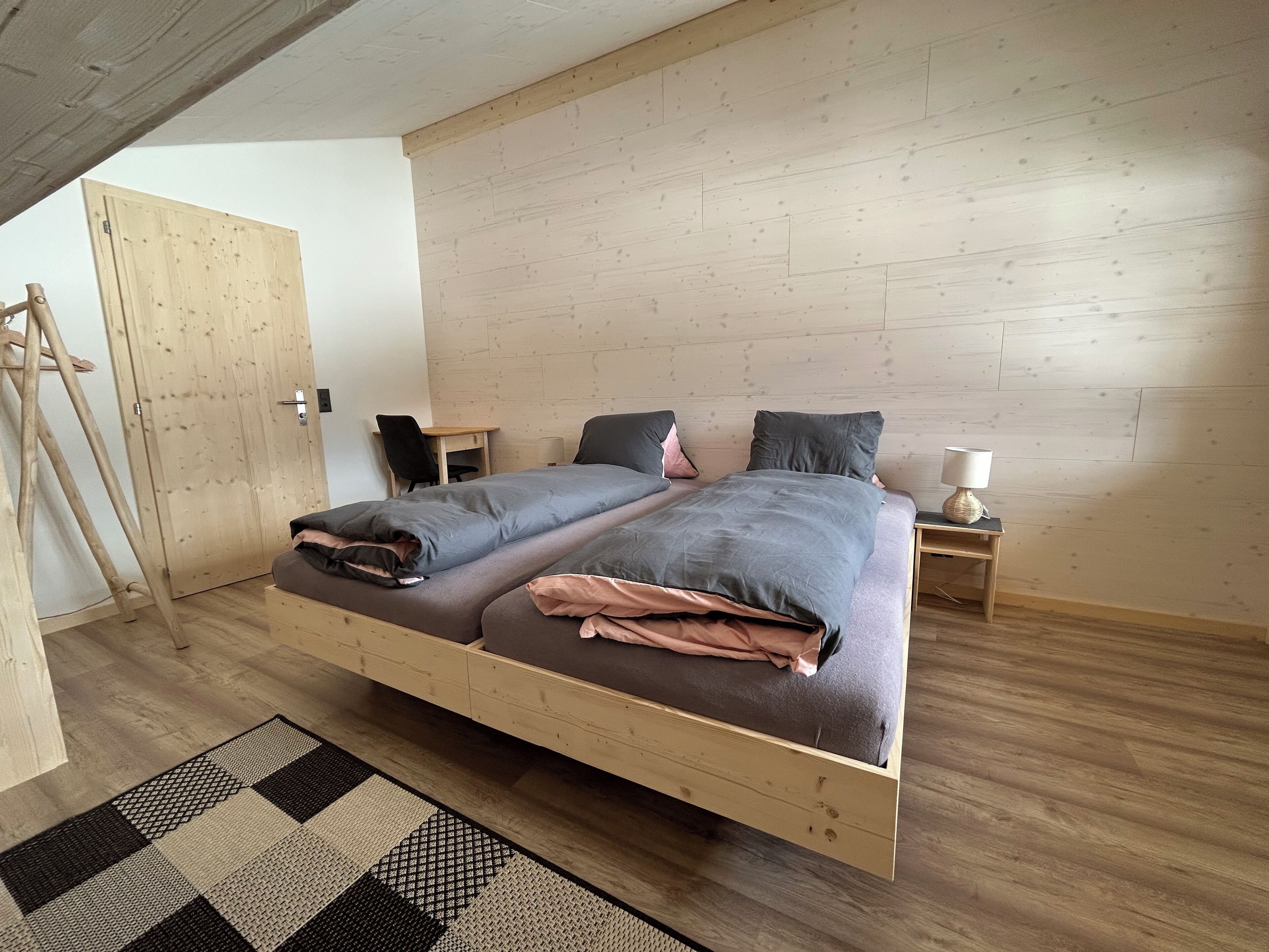 Un letto matrimoniale con struttura in legno, una scrivania con sedia, una lampada e un tappeto a quadri.
