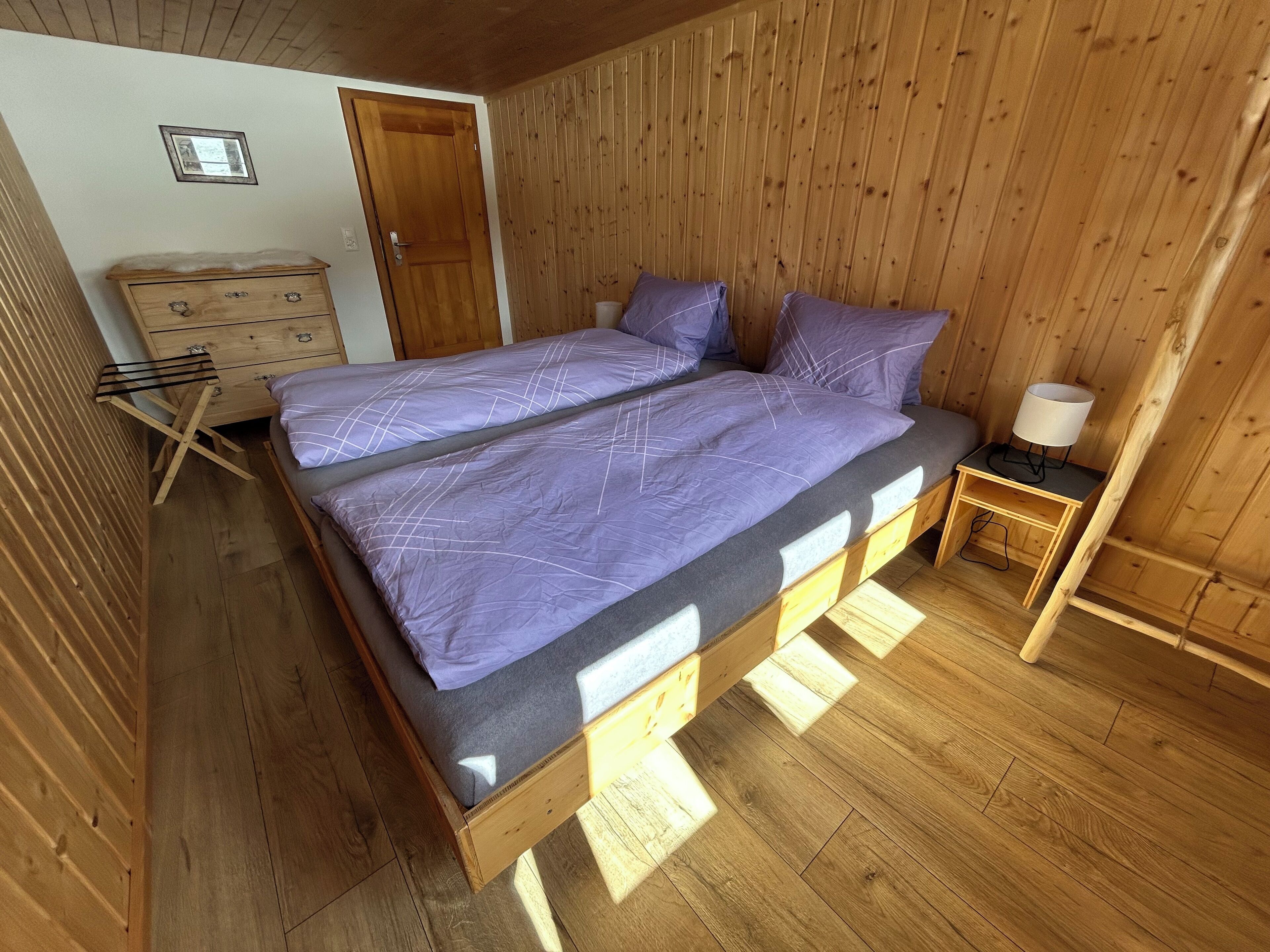 A wooden-paneled room with a bed, a dresser, and a lamp.
