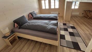 A small, cozy bedroom with two beds, a window, and a wooden floor.