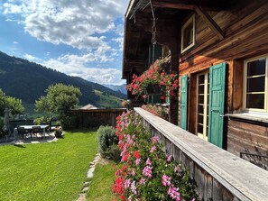 Un chalet en bois doté d’un balcon donnant sur un jardin luxuriant et un paysage montagneux.