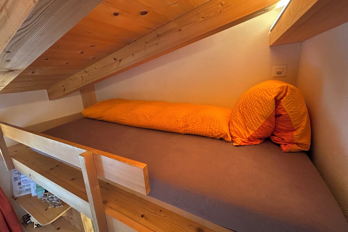 A bunk bed with an orange mattress and pillows, wooden beams, and a sloped ceiling.