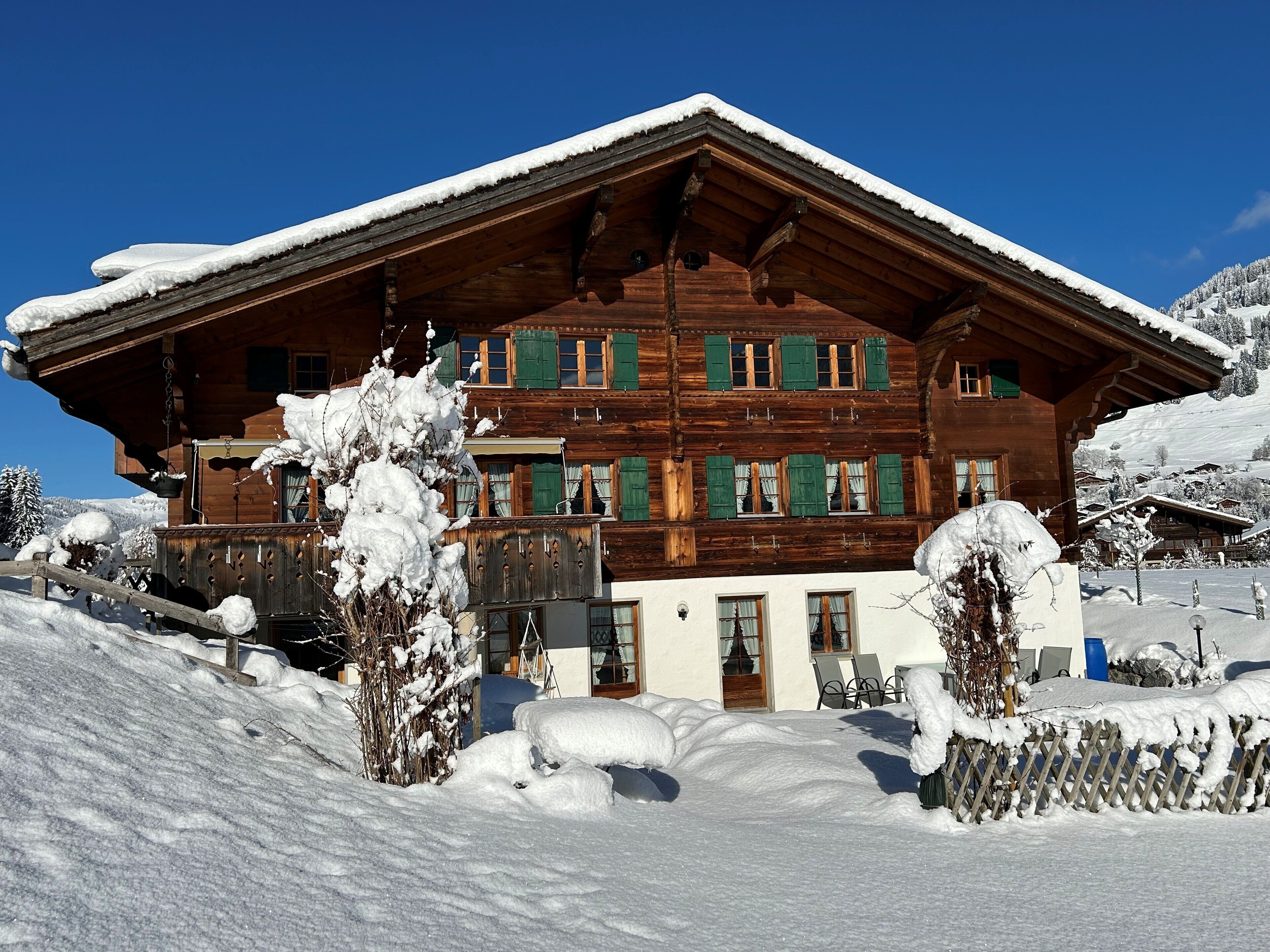 Un chalet en bois doté d’un toit à pente, de nombreuses fenêtres avec volets et d’un balcon.