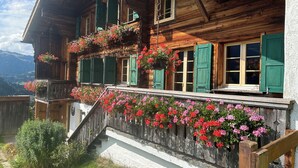 A wooden chalet with a balcony, green shutters, and hanging flower baskets.