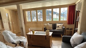 A cozy room with wooden floors, a sofa, a table with a sign, and a window with a mountain view.