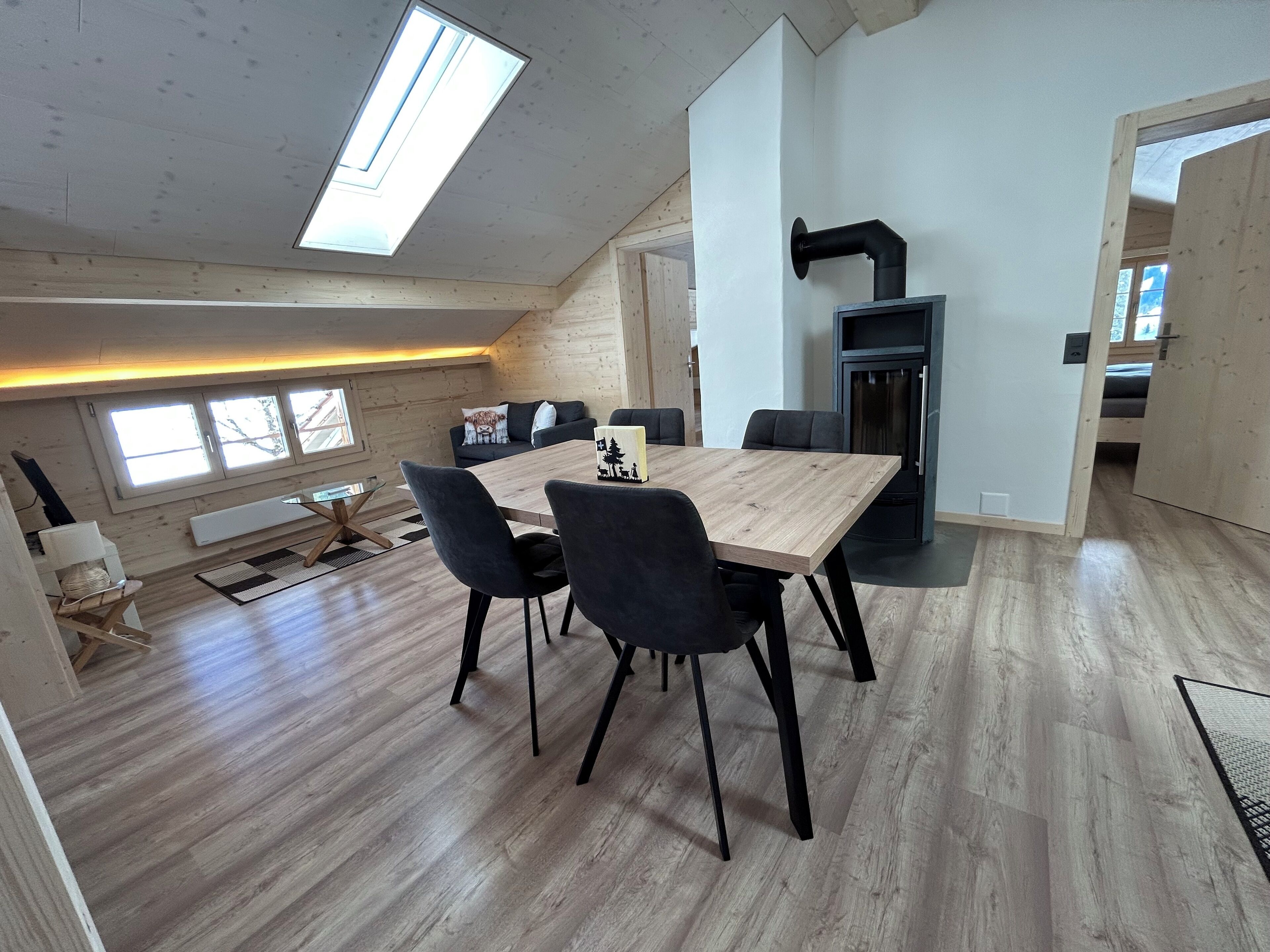A modern loft-style living space with a dining area, a fireplace, and a large skylight.