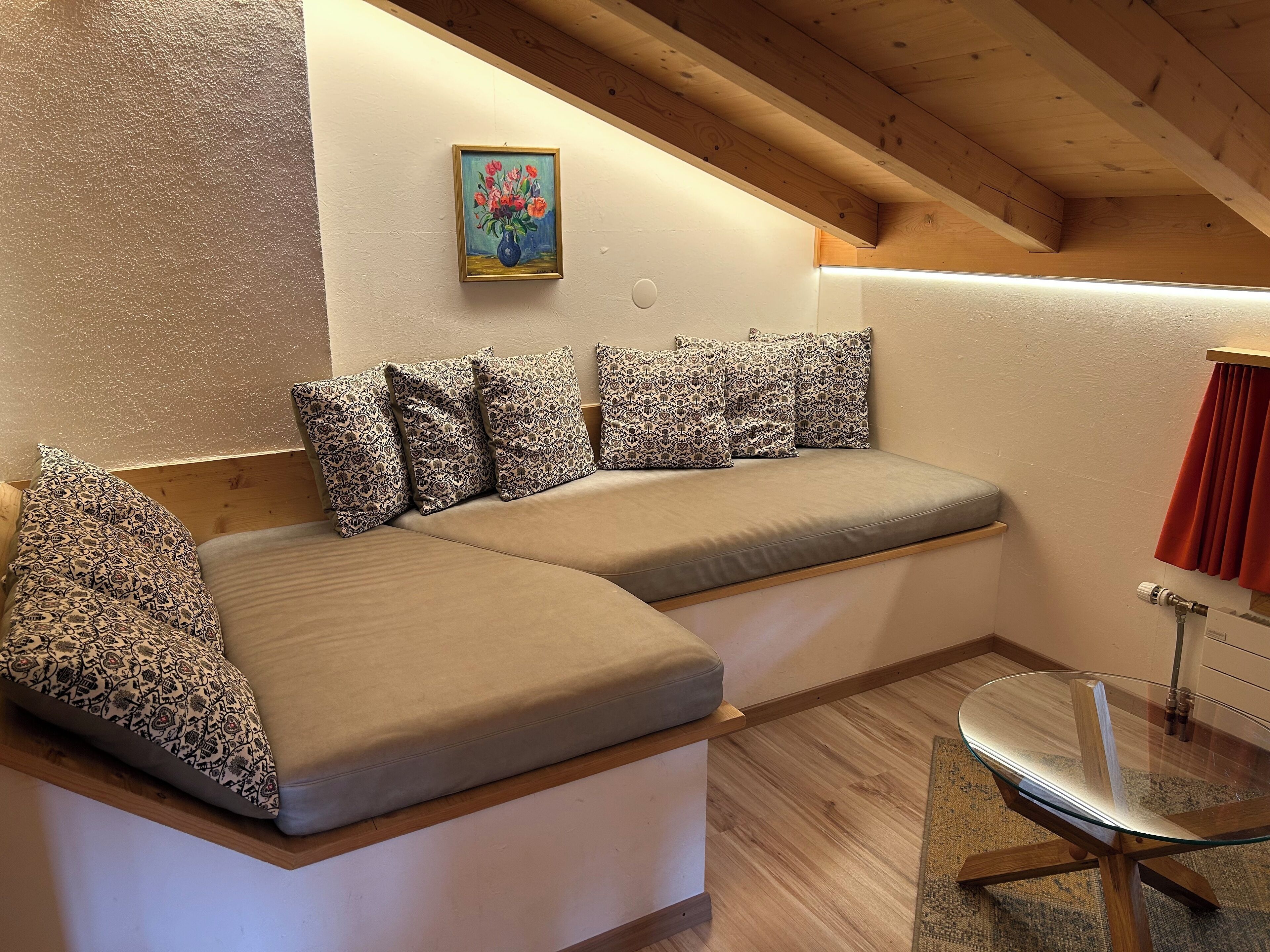 Un coin salon accueillant avec un canapé et une table en verre, un tableau au mur et un plafond en bois.