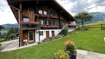 Ein traditionelles Holzchalet mit Balkonen, die mit Blumen geschmückt sind, vor einer Bergkulisse.