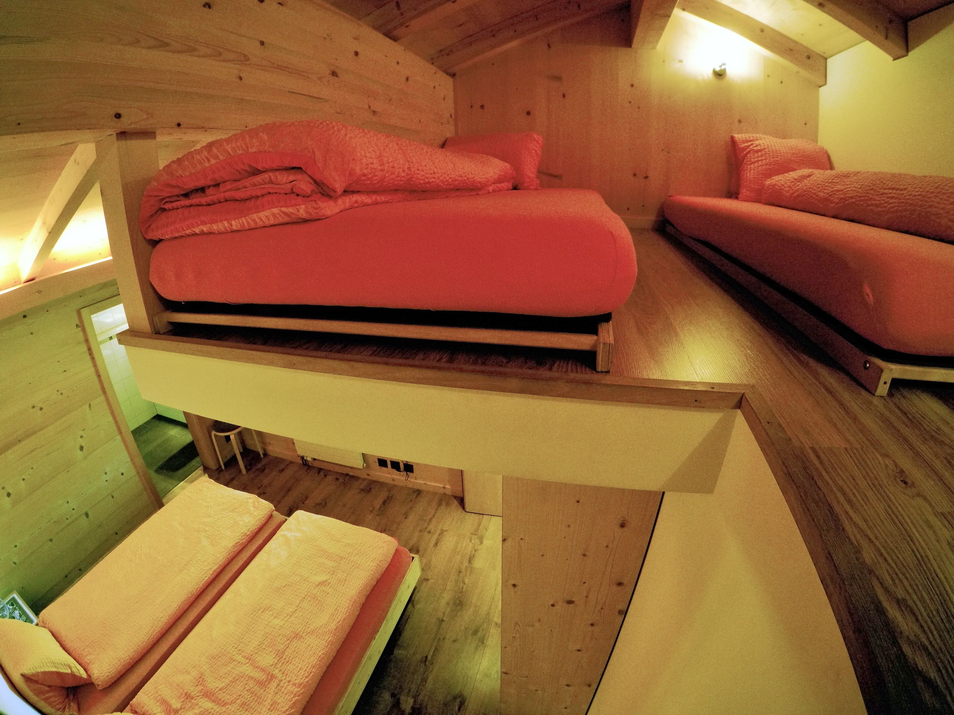 A compact room with a bed and a sofa, both with red bedding, and a wooden ceiling.