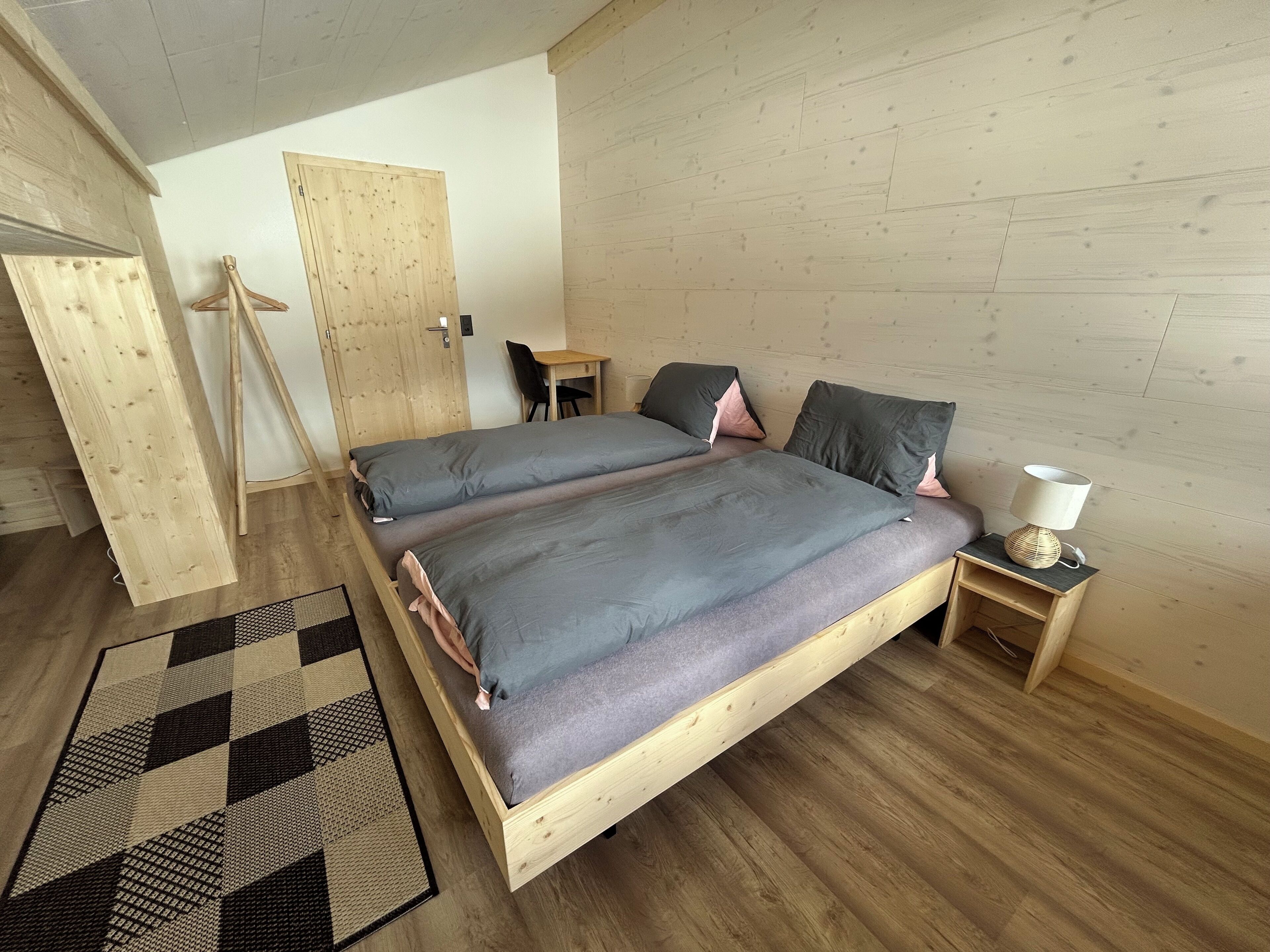 Una camera da letto con un letto in legno, una scrivania, una sedia e un comodino con una lampada.
