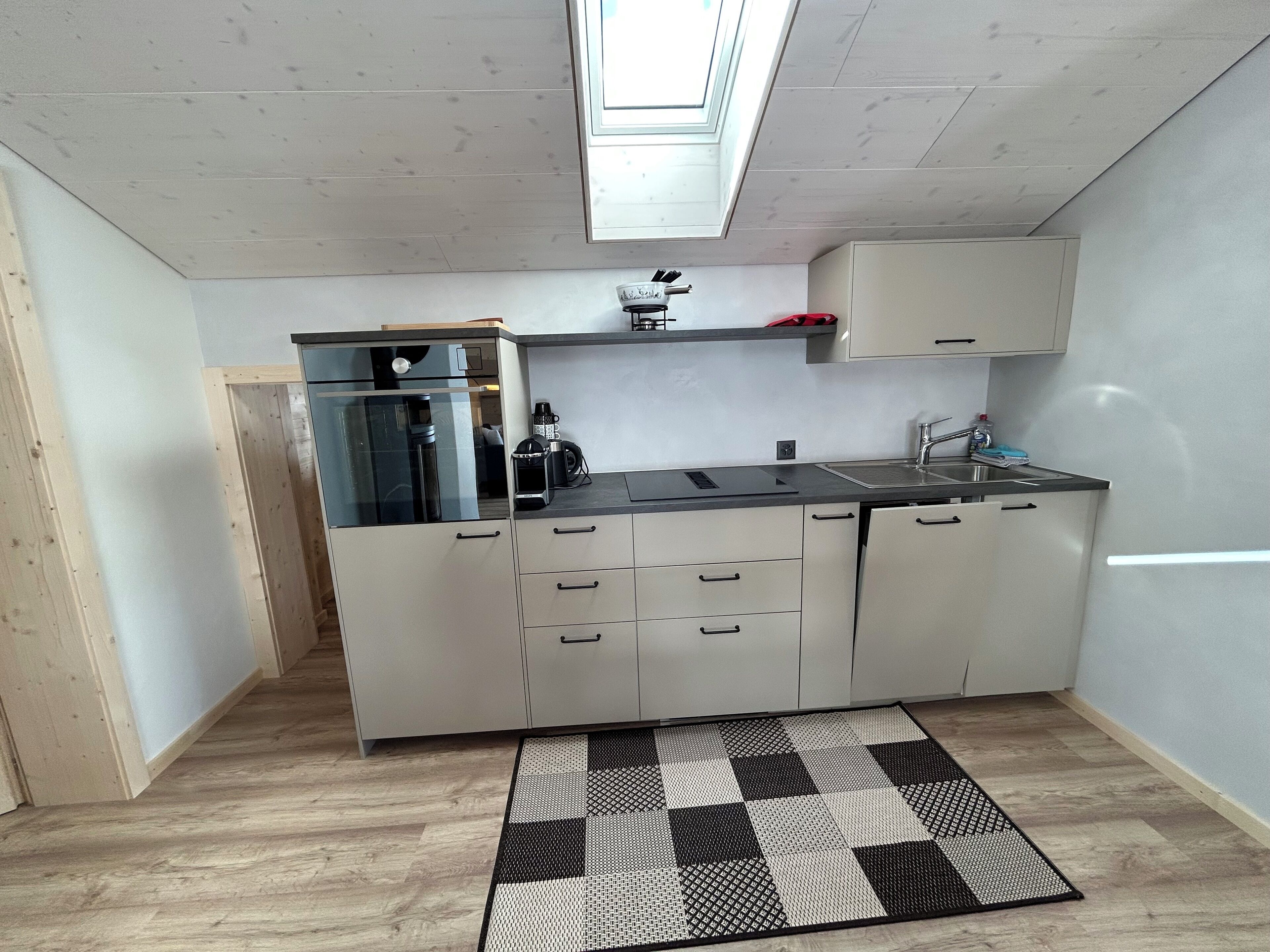 A compact kitchen with a built-in coffee machine, a sink, and a window above the countertop.