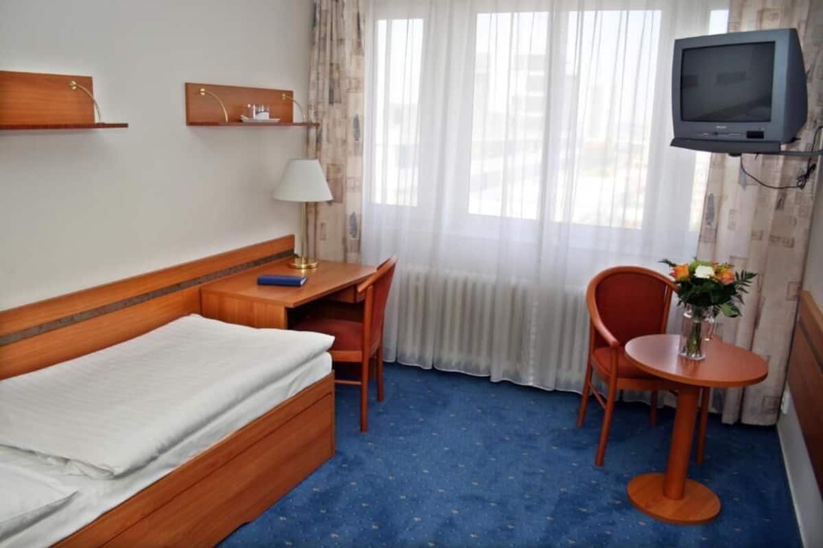 A hotel room with a bed, a desk, a chair, a TV, and a window with curtains.