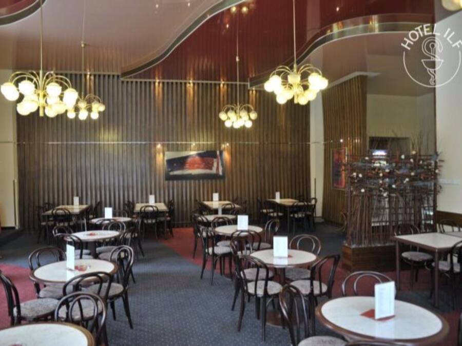 Un restaurante con mesas y sillas redondas, candelabros colgantes y un cuadro grande en la pared.