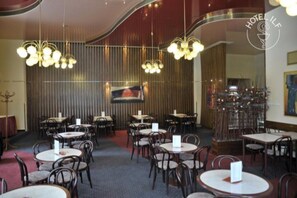 A restaurant with round tables and chairs, hanging chandeliers, and a large painting on the wall. - ILF Hotel Prague (Prague)