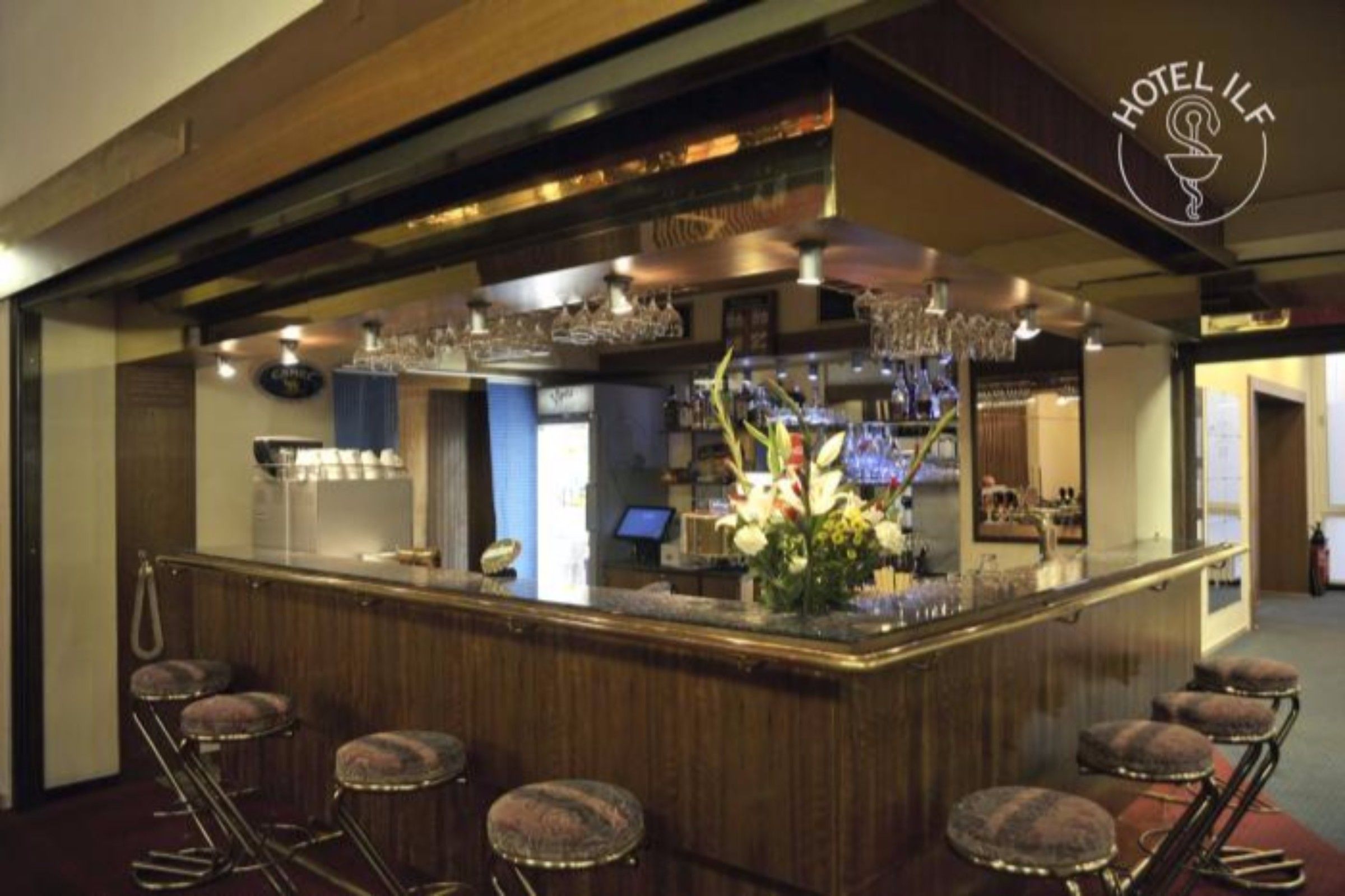 Una zona de bar con mostrador de madera, taburetes y un arreglo floral.