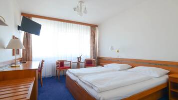 Une chambre d’hôtel avec deux lits, un bureau avec une chaise, un téléviseur fixé au mur et une fenêtre avec des rideaux.