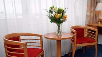 Habitación de hotel con dos sillas de madera con cojines rojos, una pequeña mesa redonda y un florero con flores.