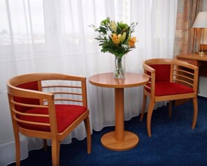 A hotel room with two wooden chairs with red cushions, a small round table, and a vase with flowers. - ILF Hotel Prague (Prague)