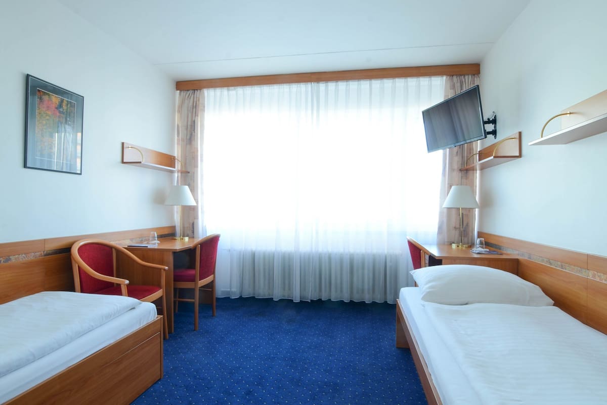 A hotel room with two single beds, a desk with a chair, a television, and a window with curtains.