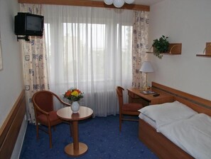 A hotel room with a bed, two chairs, a small table with a vase of flowers, a desk with a lamp, a television, and a window with curtains. - ILF Hotel Prague (Prague)