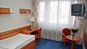 A hotel room with a bed, a desk, a chair, a TV, and a window with curtains. - ILF Hotel Prague (Prague)