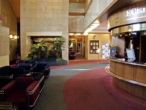 Un hall d’hôtel comprenant un comptoir d’accueil, un espace salon et une grande plante.