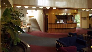 A hotel lobby with a reception desk, seating area, staircase, and potted plants. - ILF Hotel Prague (Prague)