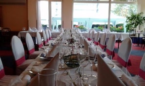A long dining table set with chairs, glasses, and cutlery, in a room with large windows and a view of greenery outside. - ILF Hotel Prague (Prague)