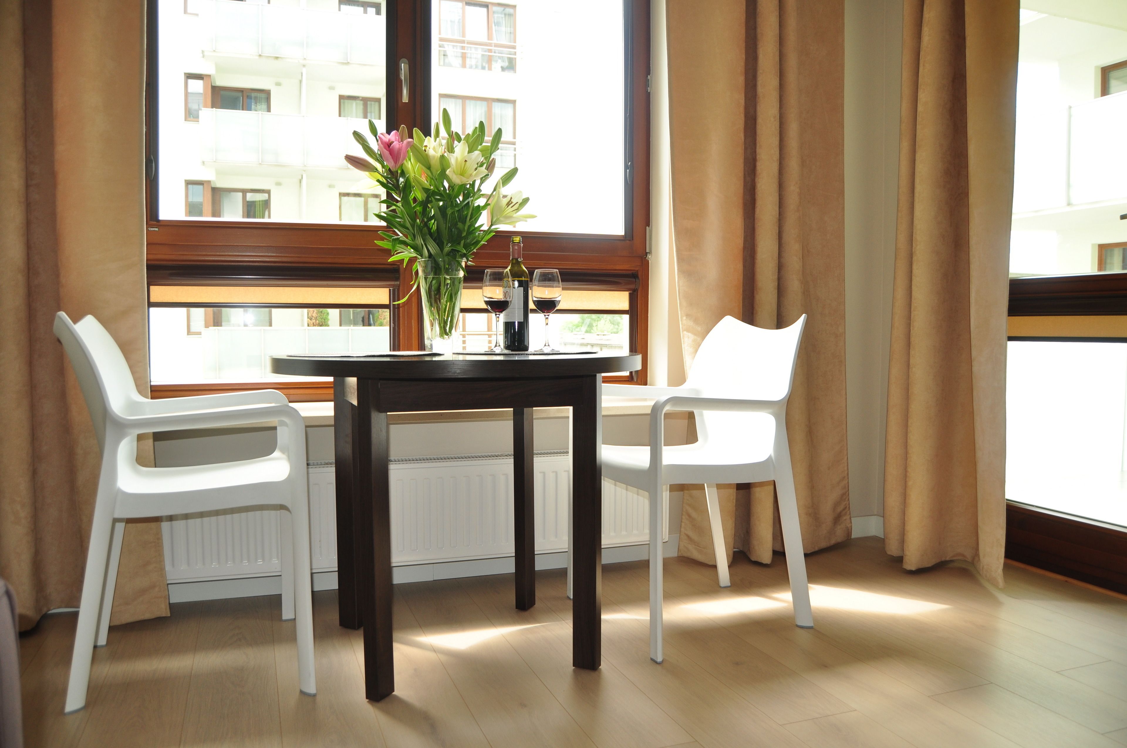 Un coin repas avec une table et deux chaises blanches, un vase avec des fleurs et deux verres à vin.