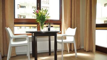 A dining area with a table and two white chairs, a vase with flowers, and two wine glasses.