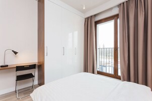 Una habitación de hotel con cama, escritorio con silla, armario y una ventana grande con cortinas.