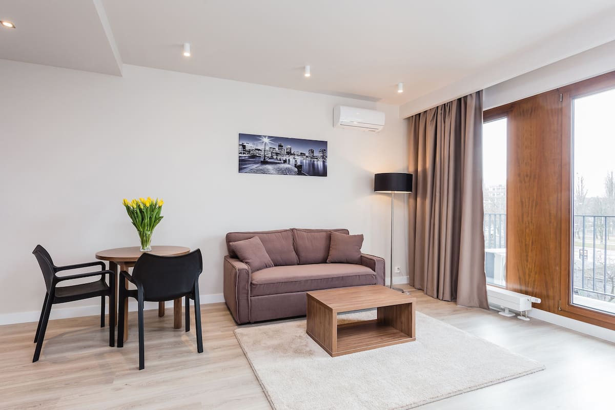 A modern living room with a brown sofa, two black chairs, a wooden coffee table, and a cityscape painting on the wall.