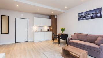 A modern apartment with a kitchenette, a living area with a sofa and coffee table, and a cityscape painting on the wall.