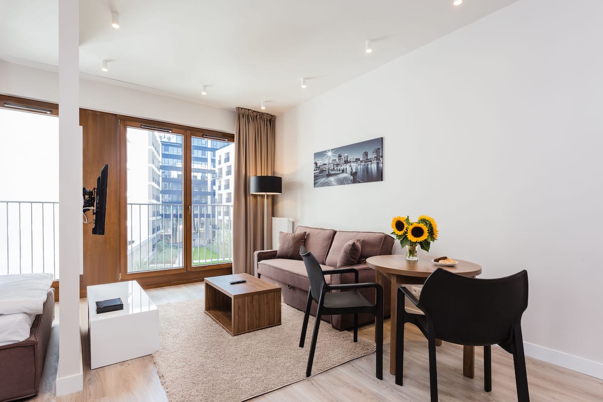 A modern living room with a sofa, a coffee table, a dining table with chairs, a TV, and a large window with curtains.