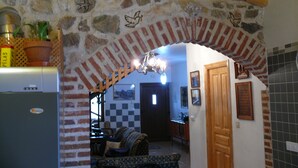 Una cocina con pared de piedra, vigas de madera en el techo y un refrigerador, además de una zona de comedor con mantel a cuadros.