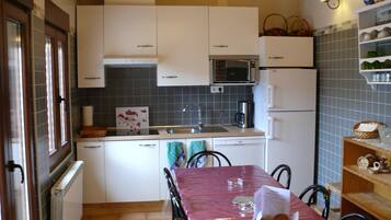Cocina compacta con armarios blancos, microondas, cafetera y mesa de comedor con sillas.