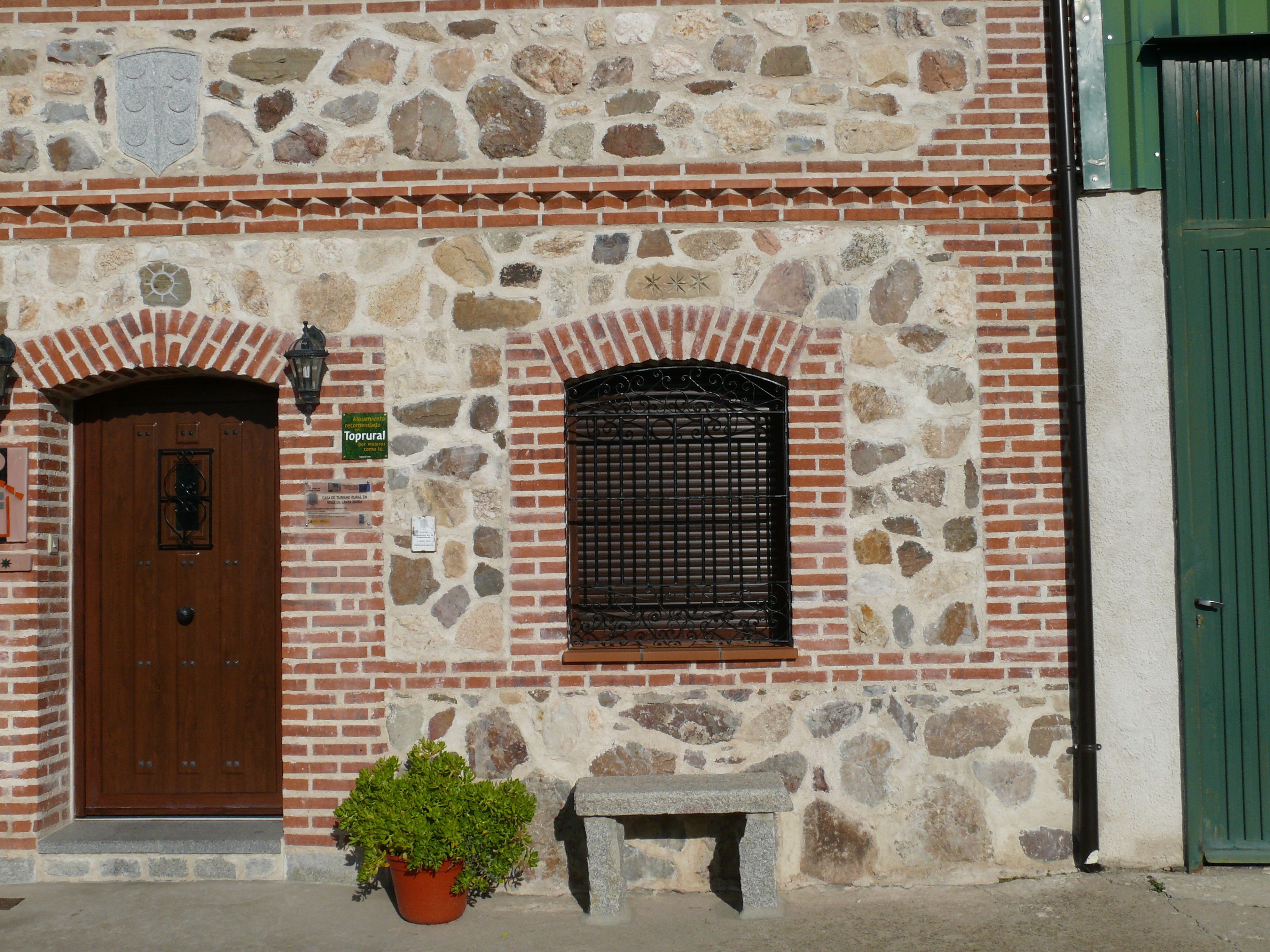 A stone building with a wooden door, a window with a metal grille, and a green door.