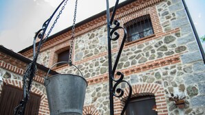 Un cubo de metal colgado de una cadena, frente a un edificio de piedra con arcos de ladrillo y una ventana.