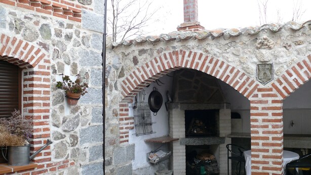 Un edificio de piedra con una chimenea de ladrillo, un arco de piedra y un pequeño espacio al aire libre con asientos.