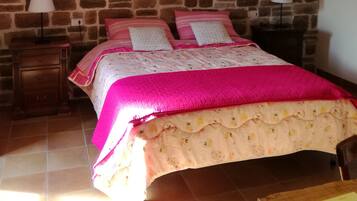 Une chambre avec un mur en pierre, un lit avec une literie rose, deux tables de chevet avec des lampes et une poutre en bois au plafond.