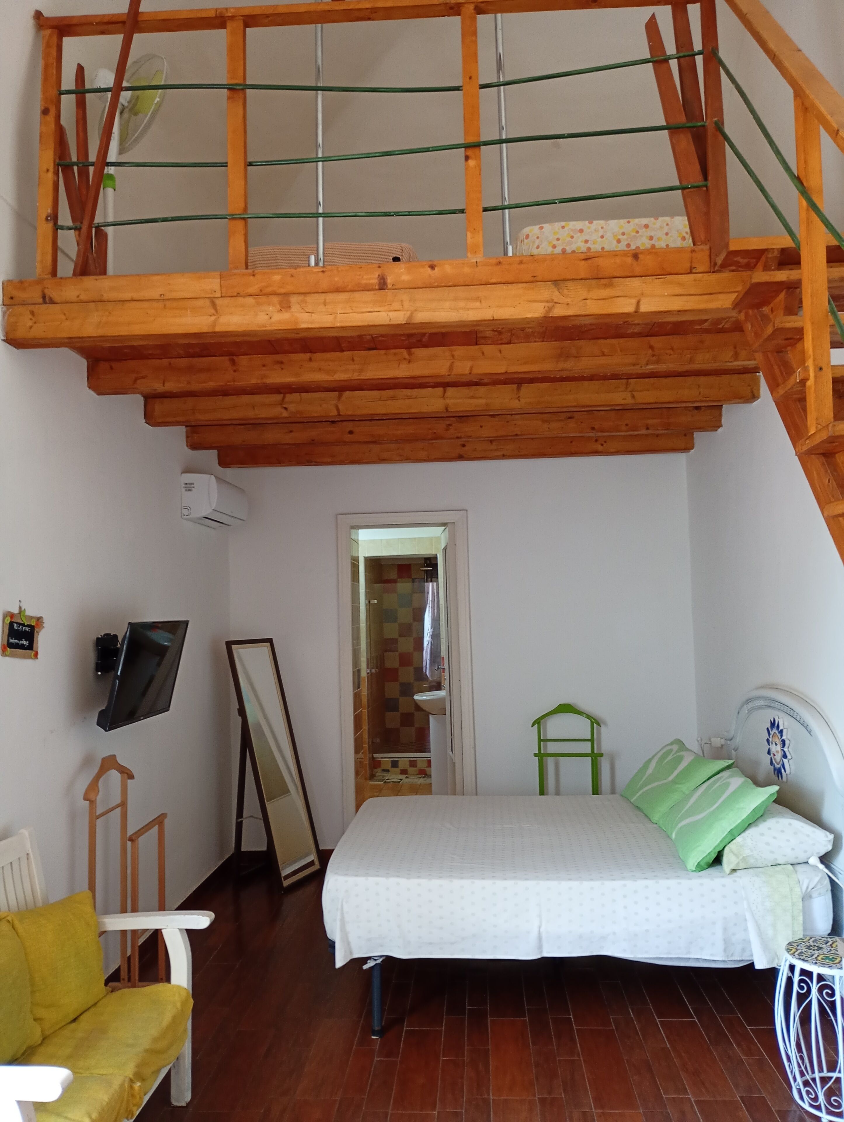 Un dormitorio con techo de madera, cama con ropa de cama verde y blanca, una mesita y una silla.