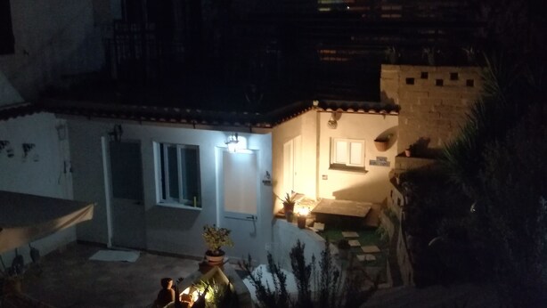 Un patio pequeño y tenuemente iluminado, con suelo de baldosas, algunas plantas en macetas y una pequeña zona de estar al aire libre.