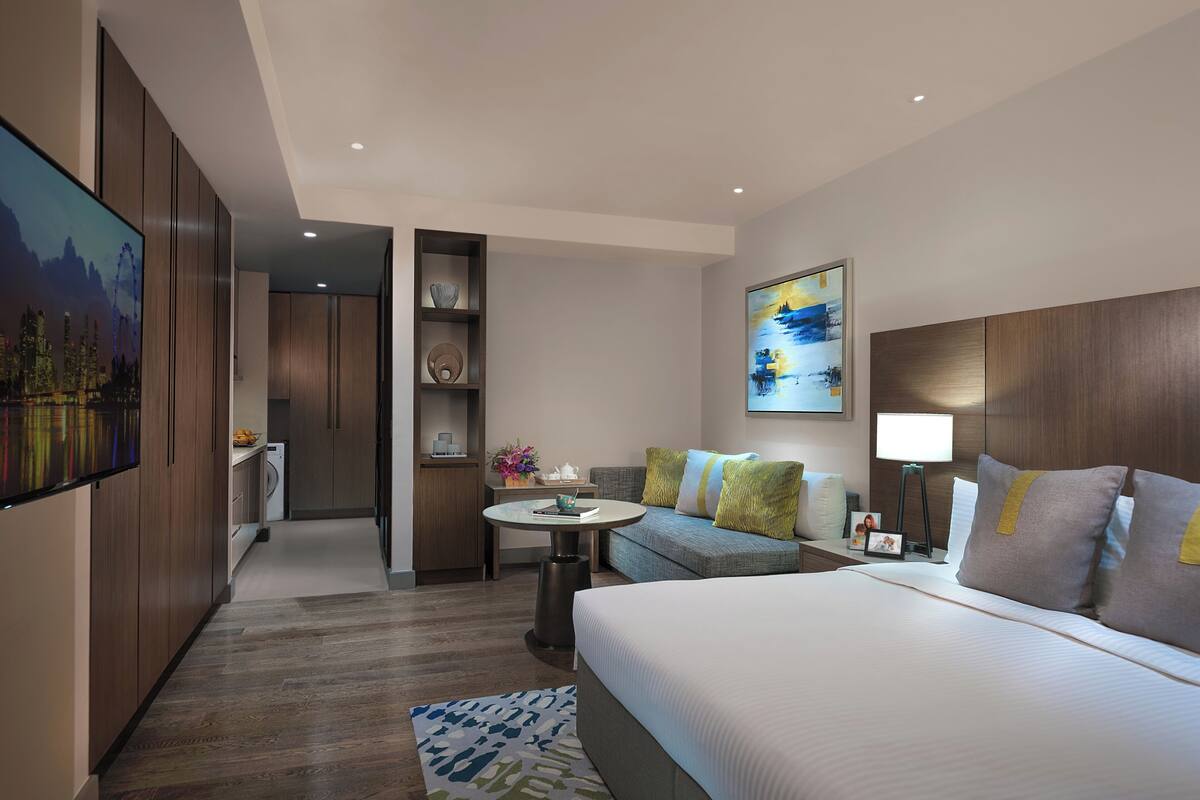 A hotel room with a bed, a sofa, a desk, a TV, and a painting on the wall.