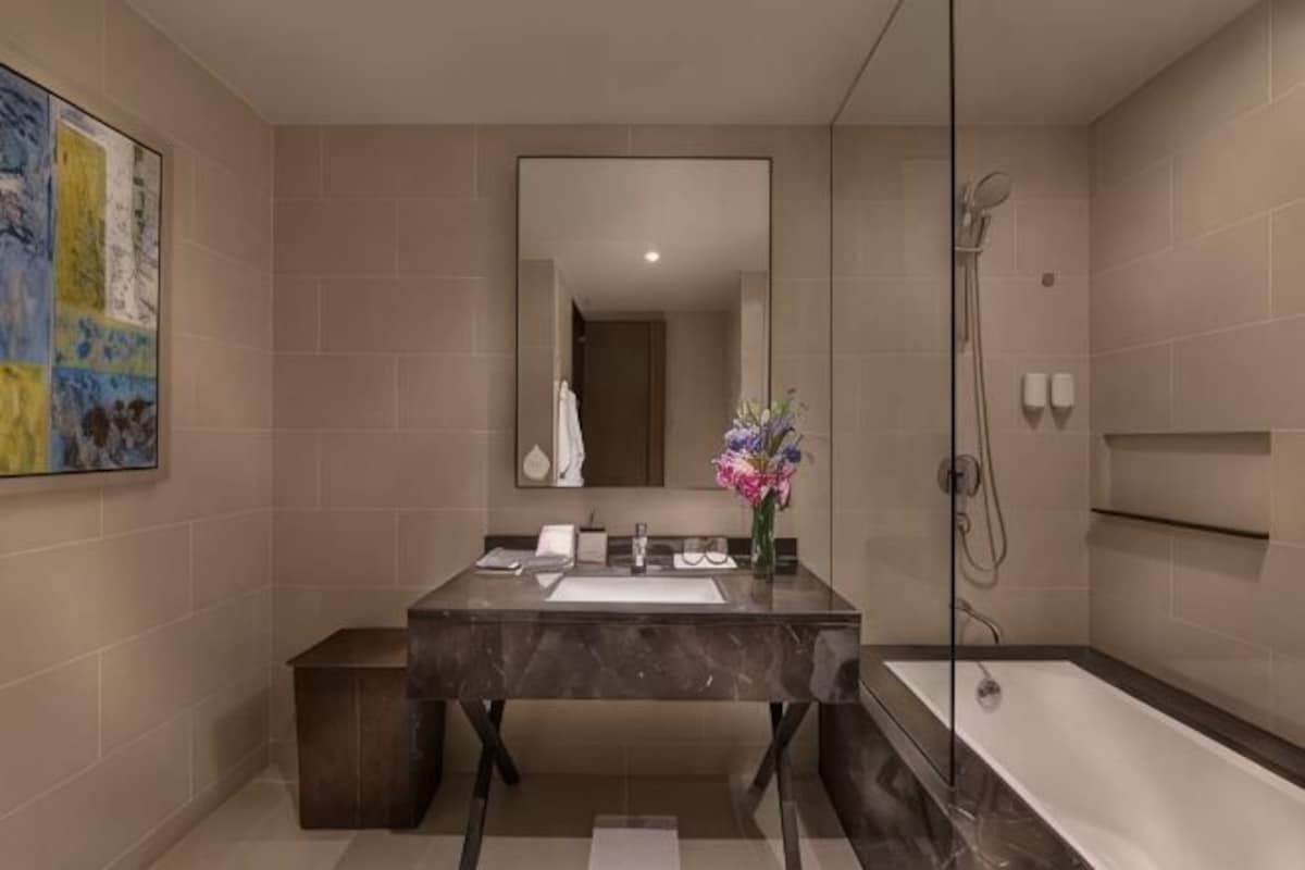 Un baño moderno con lavamanos de mármol, un espejo grande, ducha y una obra de arte enmarcada en la pared.
