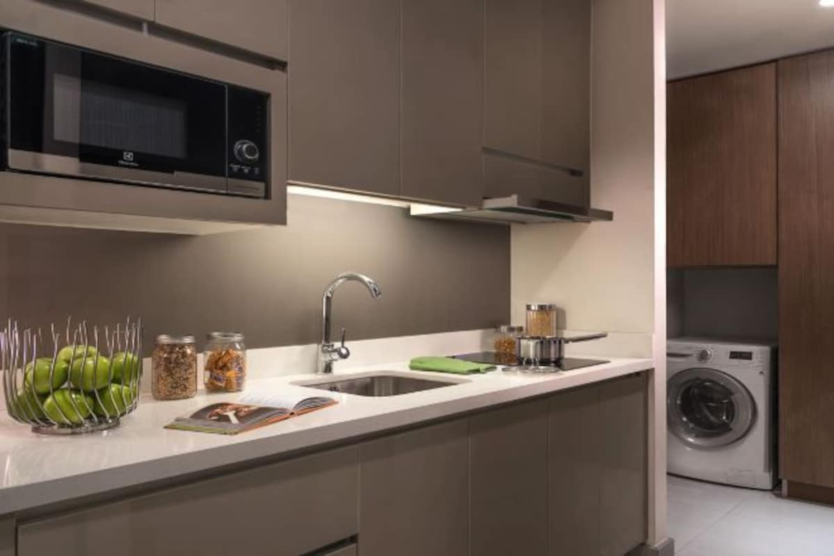 Una cocina moderna con microondas integrado, pileta de acero inoxidable y lavadora en la habitación contigua.